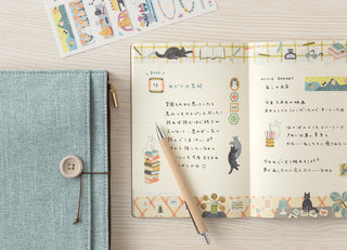 Notebook with decorative pages on a wooden surface, next to a pen and another notebook.