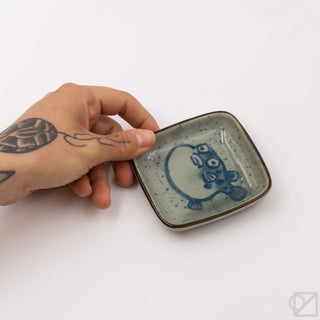 Ceramic puffer-fish dish held at an angle, blue puffer fish graphic on speckled glaze