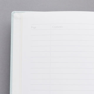 A close-up of an open lined notebook showing a blank page with faint 'Page' and 'Contents' headers, set against a neutral gray background.