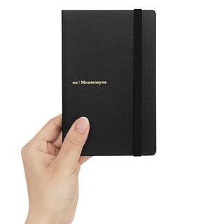 A hand holding a hardcover notebook with a gold-foiled '868 | Mnemosyne' logo on the front, set against a plain white background.