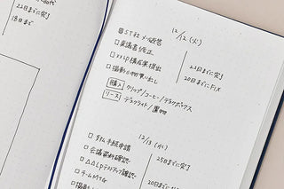 A close-up of an open dot grid notebook showing handwritten Japanese notes with date and to do tasks