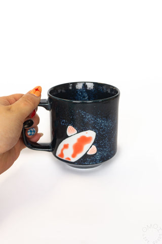 Dark blue mug with a fish design held by a hand on a white background