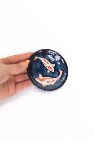 Hand holding a small ceramic dish with Koi fish design on a white background