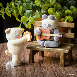 Two plush toys, one playing a guitar and the other holding a tamborine, on a wooden bench with green plants in the background.