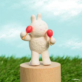 White rabbit figurine with maracas on a wooden stand against a green grass and blue sky background.
