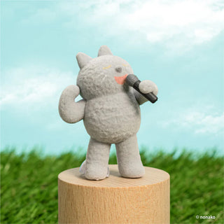 Gray plush animal toy with a microphone on a wooden stand against a grassy background