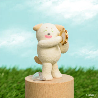 Toy figure of an animal playing a tambourine on a wooden stand with a grassy field and blue sky background.
