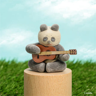 Toy panda playing a guitar on a wooden pedestal with a grassy background