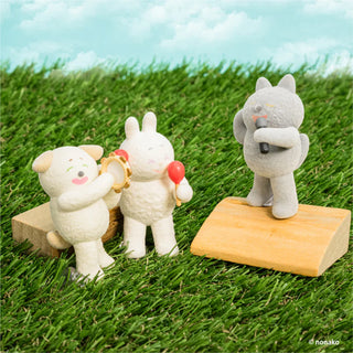 Three small animal figurines playing instruments on wooden stands with a grassy background