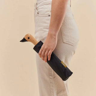Person holding a black umbrella with a wooden duck handle against a beige background