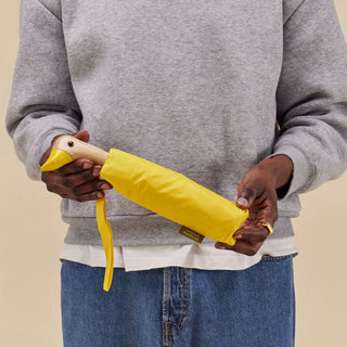 Person holding a yellow umbrella with a neutral background