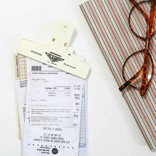Penco binder clip holding receipts, and eyeglasses on a textured surface on a white background