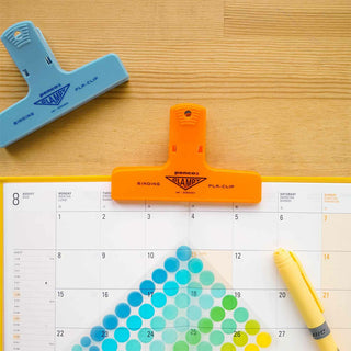 Orange and blue paper clips on a planner with a yellow pen
