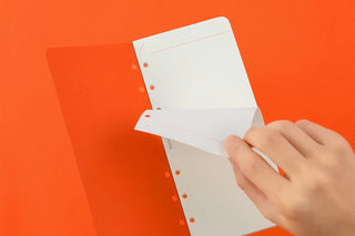 Hand holding a white sheet of paper with holes on an orange background