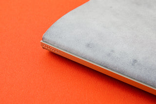 Side of blueish gray leather binder with silver details on orange background