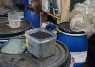 Container of dark powder on a metal surface with various containers and items in the background