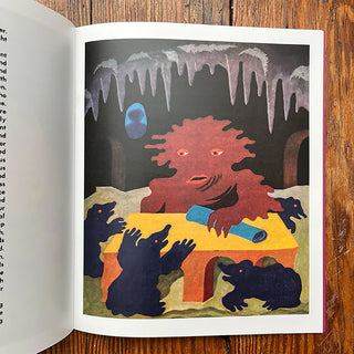 Illustrated book page with a red creature and black creatures on a table against a cave background.