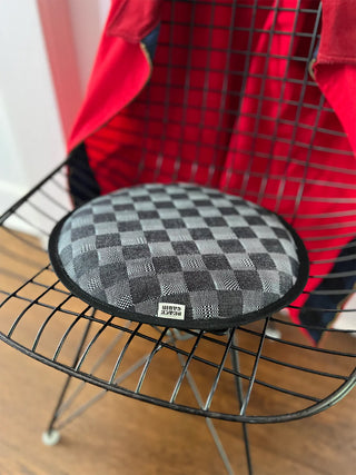 Round black and gray checkered cushion on a wire chair with a red jacket in the background.