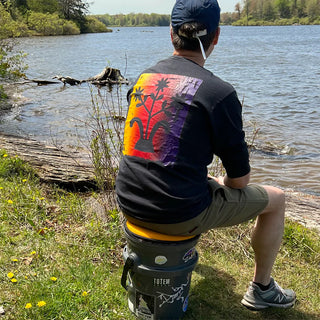 Person sitting by a lake on seat cushion on a bucket