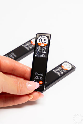 Hand holding a Pentel Ain mechanical pencil with two additional pencils on a white background