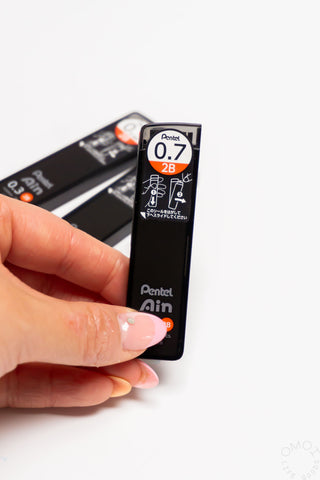 Hand holding a black Pentel lead pencil refill on a white background