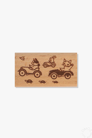 Wooden stamp with cats and a rabbit driving alongside turtles and birds on a white background