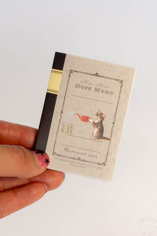 Small notebook with a cat illustration held by a hand on a light background