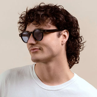 RAEN round sunglasses on person, black frame with dark lenses in profile