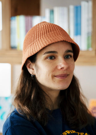 Close up of person wearing Rototo Apricot hat with books in the background