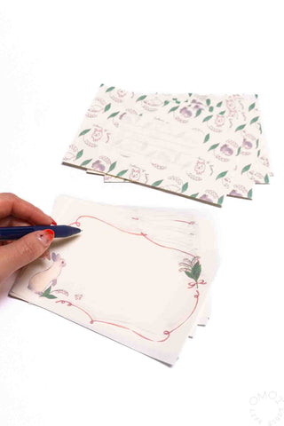 Floral-patterned paper and a rabbit design with a hand holding a pen on a white background