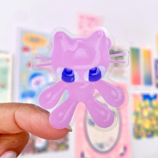 Pink cat-shaped sticker held by a hand with a colorful background