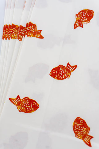 Close up of white paper bags with red fish patterns on a white background