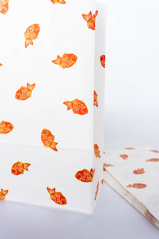 Close up of white paper bags with red fish patterns on a white background