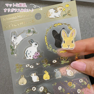 Sheet of rabbit-themed stickers with a hand holding it, featuring the artist 'Schinako Moriyama'.