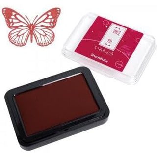 A Shachihata ink pad in a rectangular case with dark red ink, shown alongside its clear plastic packaging and a red butterfly stamp design on a white background.
