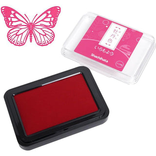ink pad in a case shown with its pink branded lid on a white background, plus a pink butterfly stamp design in the upper left.