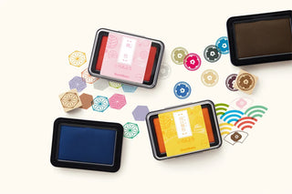 Three ink pads in different colors surrounded by colorful geometric wooden stamps and matching ink pads on a light background.