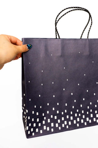 Hand holding a dark paper bag with white geometric pattern on a white background