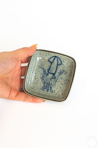 Hand holding a small ceramic dish with a blue squid design on a white background