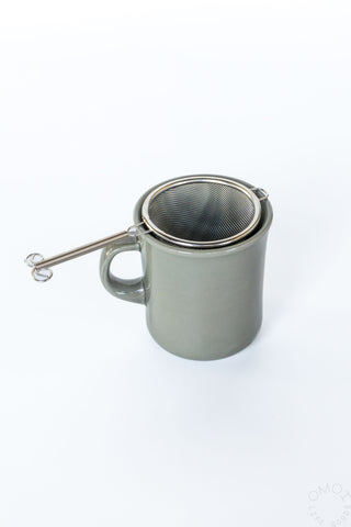 Gray mug with a metal mesh tea strainer on a white background
