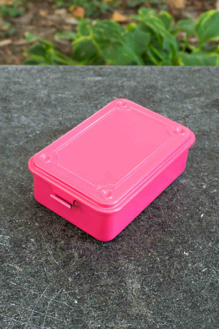 Pink toolbox on a textured surface with greenery in the background