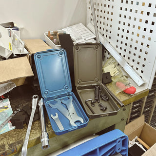 Two toolboxes, one blue and one brown, on a cluttered workbench with tools and equipment around.