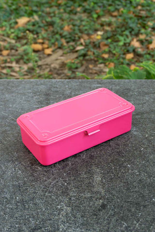 Pink toolbox on a gray surface with a green outdoor background