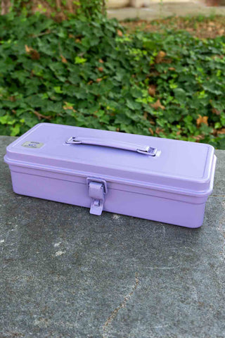 Purple metal toolbox on a stone surface with greenery in the background