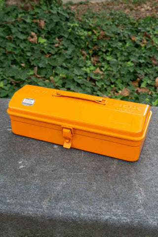 Orange toolbox on a stone surface with green foliage in the background