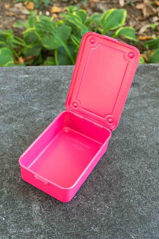 Pink toolbox with a lid on a stone surface with greenery in the background