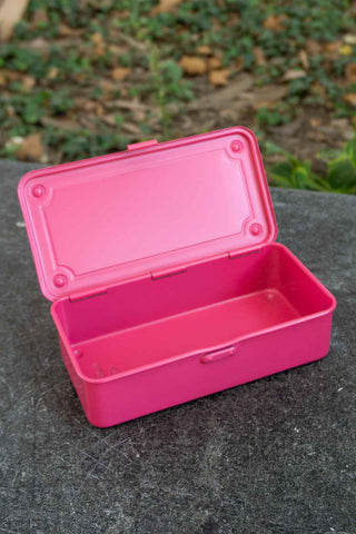 Pink toolbox with a lid on a dark surface with greenery in the background