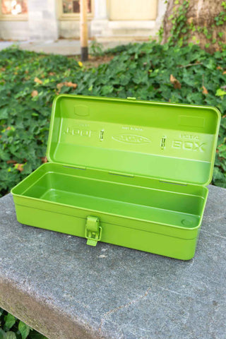 Green tool box on a stone surface with greenery in the background