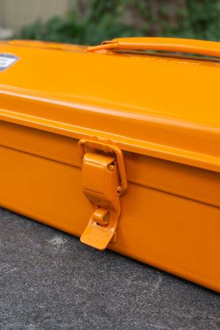 Orange toolbox on a gray surface with greenery in the background