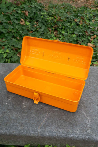 Orange toolbox on a stone surface with green foliage in the background